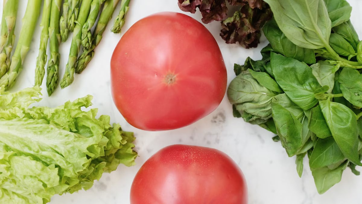 A vibrant collection of fresh vegetables including tomatoes, asparagus, and leafy greens on a marble surface.